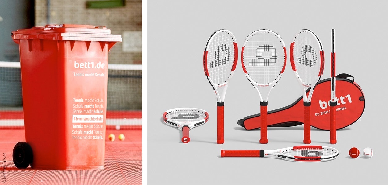 Foto: Links eine rote Tonne mit der Aufschrift „bett1.de – Tennis macht Schule“; rechts mehrere Tennischläger, eine Schlägertasche mit der Aufschrift „bett1.de – Du spielst Tennis.“ und je ein roter und weißer Tennisball.